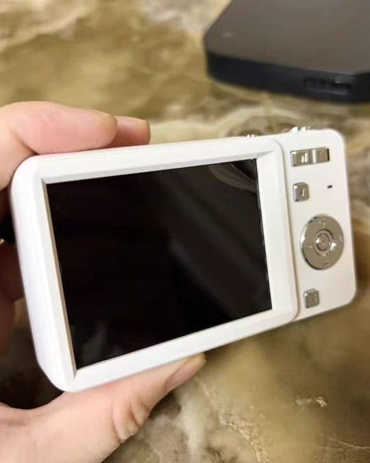 a hand holding a silver slide camera against silver satin