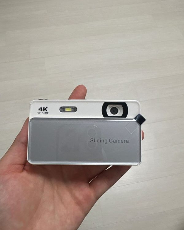 a hand holding a silver slide camera with a black lens
