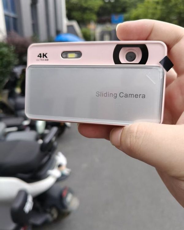 a hand holding a pink and silver slide camera on a city street