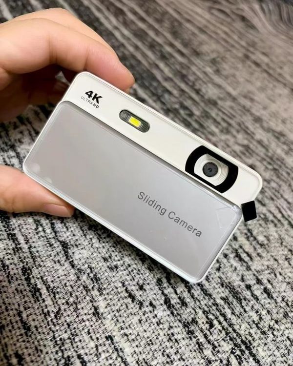 a silver slide camera held in a hand over a grey rug