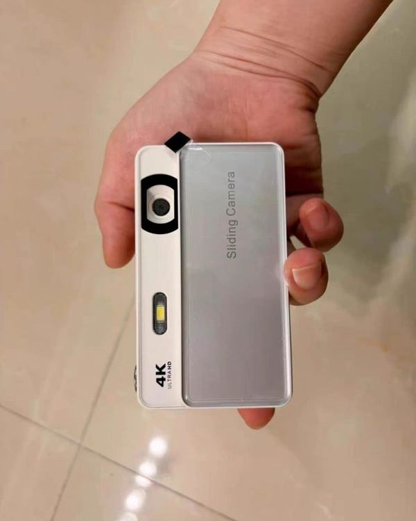 a hand holding up a white and silver slide camera against a tiled floor