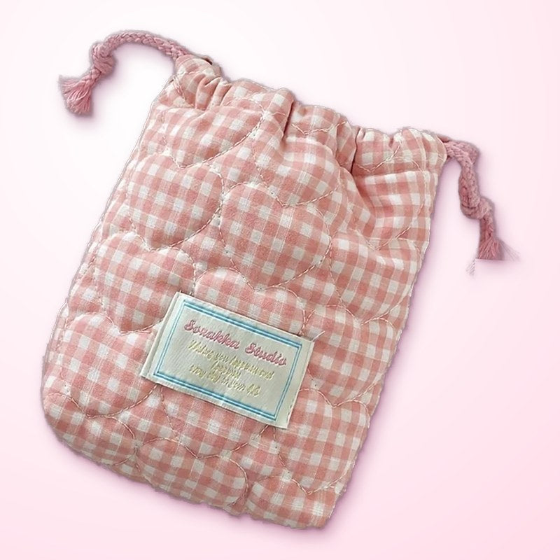 a pink gingham drawstring carry bag on a pink cloth
