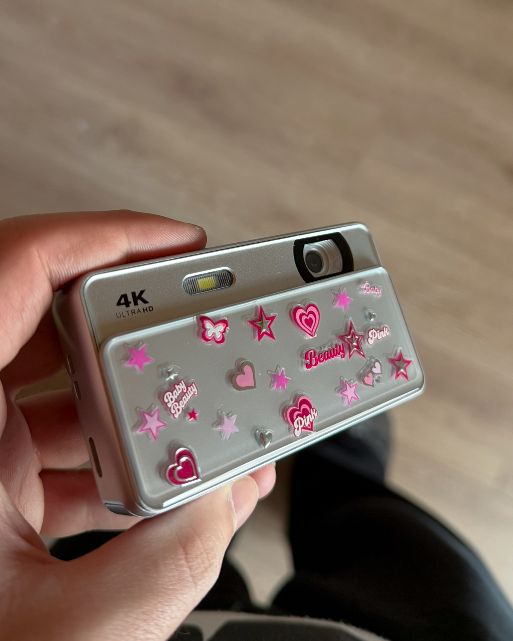 a silver slide camera covered in pink stickers, held in a hand