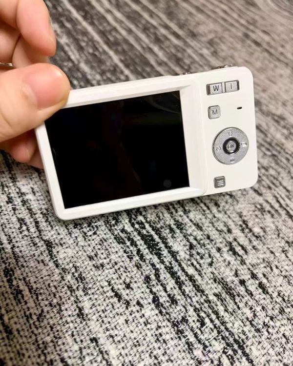 a hand holding an open camera box with a silver camera inside