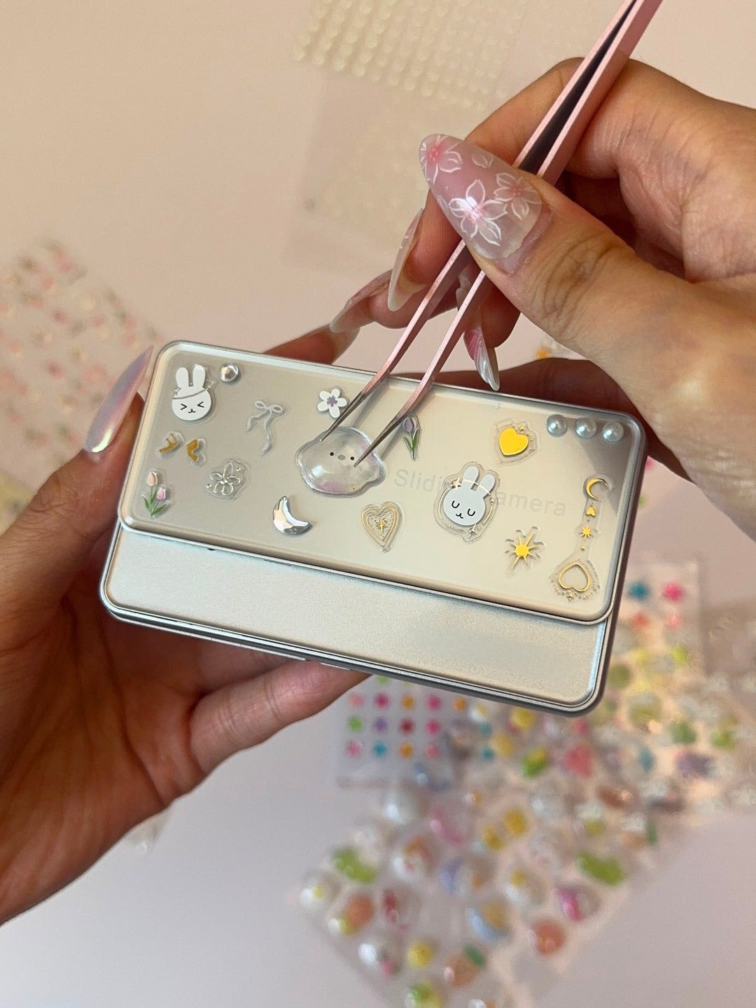 two hands decorating the slider of a slide camera with tiny stickers and pink tweezers